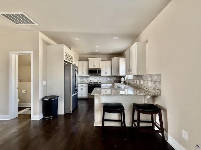 kitchen featuring visible vents, appliances with stainless steel finishes, a sink, light stone countertops, and a peninsula