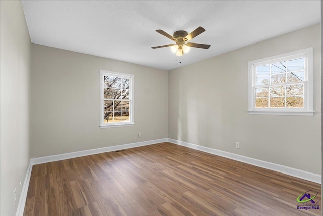 empty room with ceiling fan, a textured ceiling, baseboards, and wood finished floors