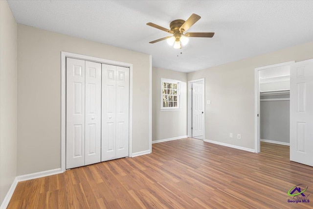 unfurnished bedroom with a closet, a ceiling fan, a textured ceiling, wood finished floors, and baseboards