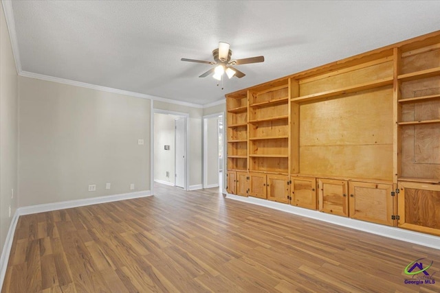 empty room with a ceiling fan, crown molding, baseboards, and wood finished floors