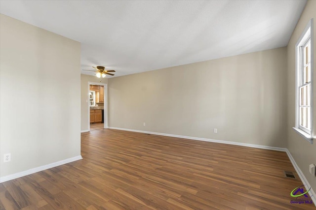 empty room with dark wood-style floors, visible vents, ceiling fan, and baseboards