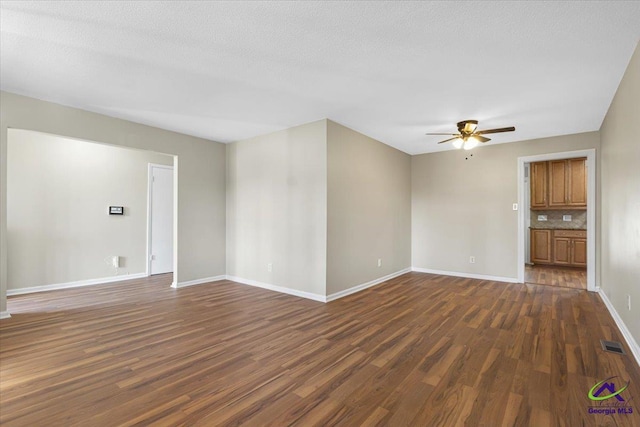 empty room featuring baseboards, visible vents, ceiling fan, dark wood-style flooring, and a textured ceiling