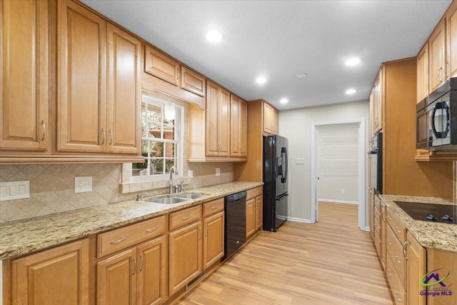 kitchen featuring a sink, light stone countertops, black appliances, light wood finished floors, and tasteful backsplash