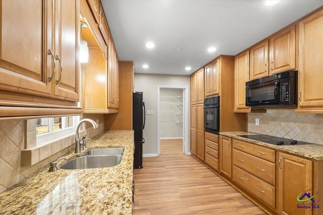 kitchen featuring baseboards, light wood-style floors, light stone countertops, black appliances, and a sink