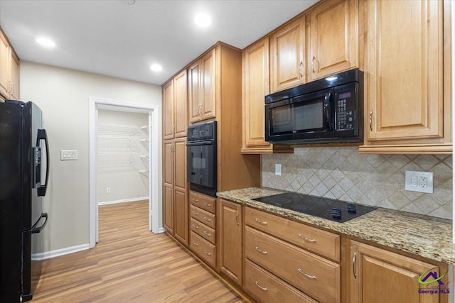 kitchen with backsplash, light wood-style flooring, black appliances, and light stone countertops