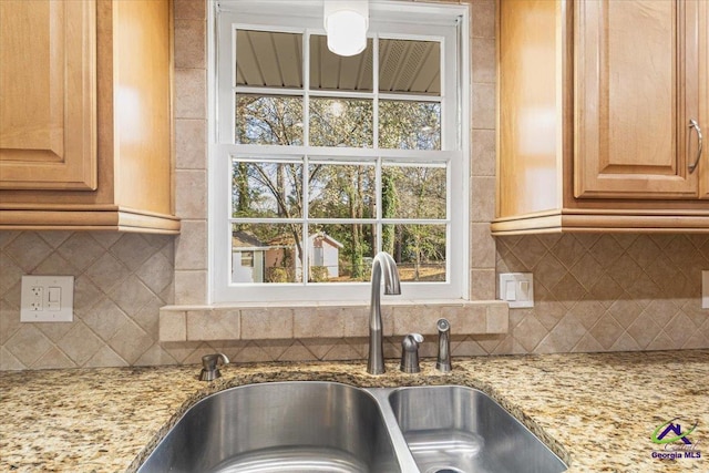 kitchen with light stone countertops, decorative backsplash, and a sink