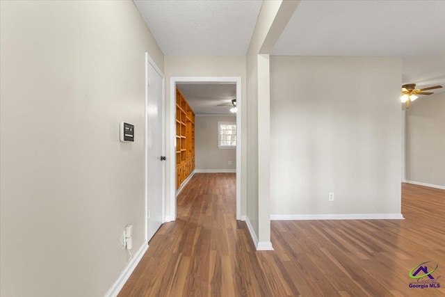 hallway with a textured ceiling, wood finished floors, and baseboards