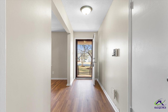 doorway to outside featuring a textured ceiling, dark wood-style flooring, and baseboards