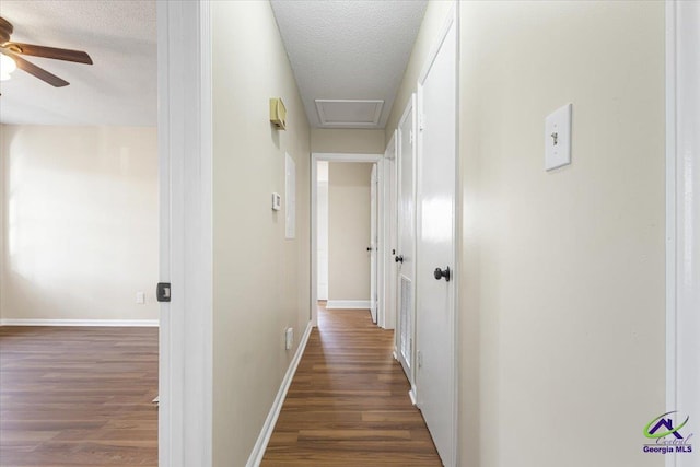 corridor with dark wood-style floors, a textured ceiling, attic access, and baseboards