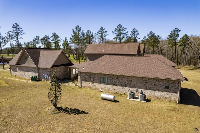 view of home's exterior with brick siding, roof with shingles, a lawn, and central air condition unit