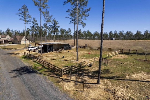 view of yard with an outbuilding, a rural view, fence, driveway, and an exterior structure