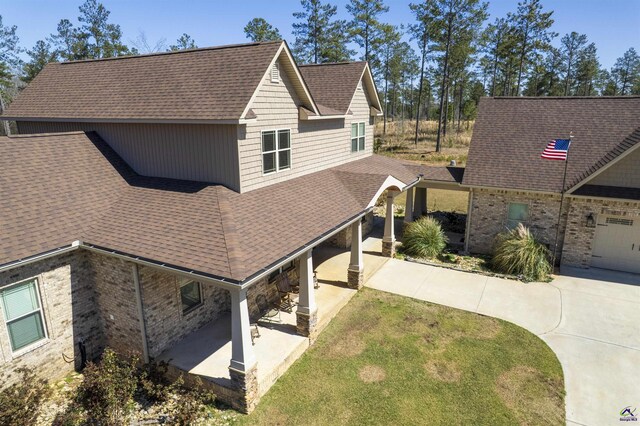 view of front of home featuring roof with shingles, brick siding, concrete driveway, a patio area, and a front lawn