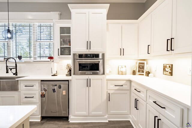 kitchen with stainless steel appliances, a sink, white cabinets, light countertops, and glass insert cabinets