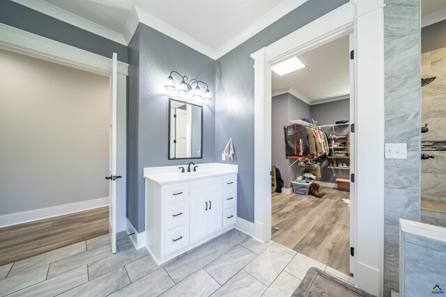 bathroom with a walk in closet, crown molding, a tile shower, vanity, and baseboards