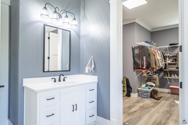 bathroom with wood finished floors, vanity, baseboards, ornamental molding, and a walk in closet