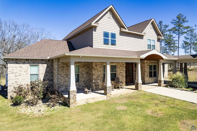 view of front of house featuring a patio area, brick siding, a front yard, and a shingled roof