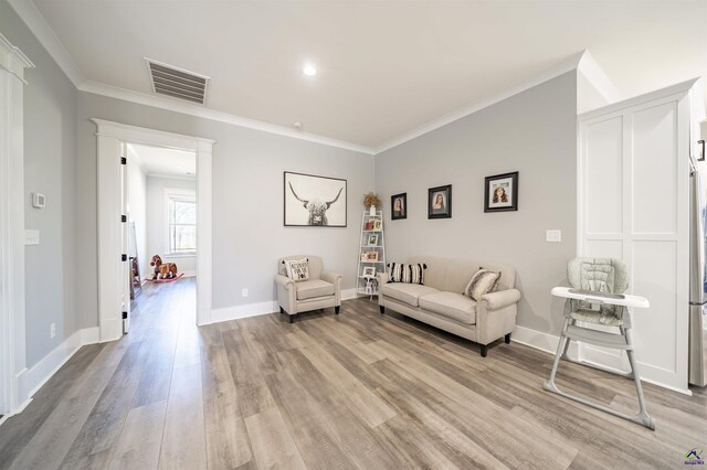 living area featuring light wood finished floors, baseboards, visible vents, and ornamental molding