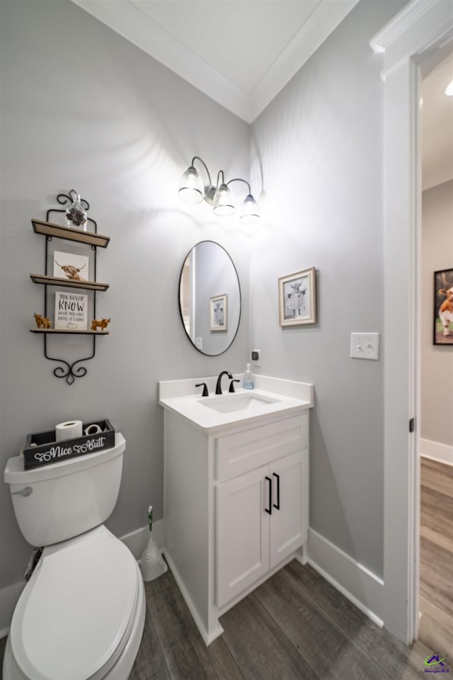 bathroom featuring toilet, wood finished floors, vanity, baseboards, and ornamental molding