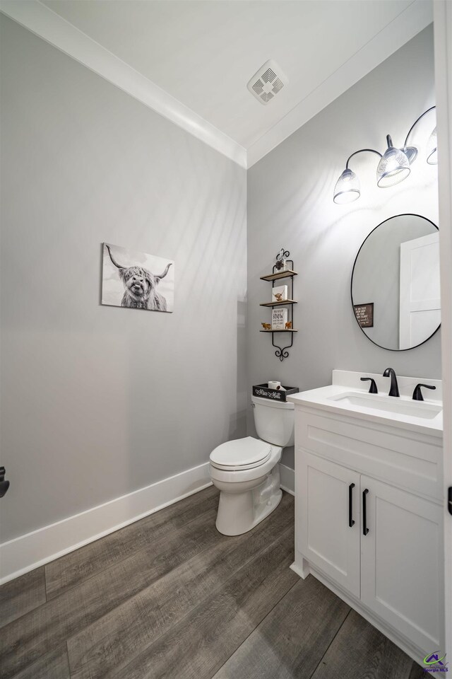 half bathroom featuring visible vents, toilet, ornamental molding, wood finished floors, and vanity