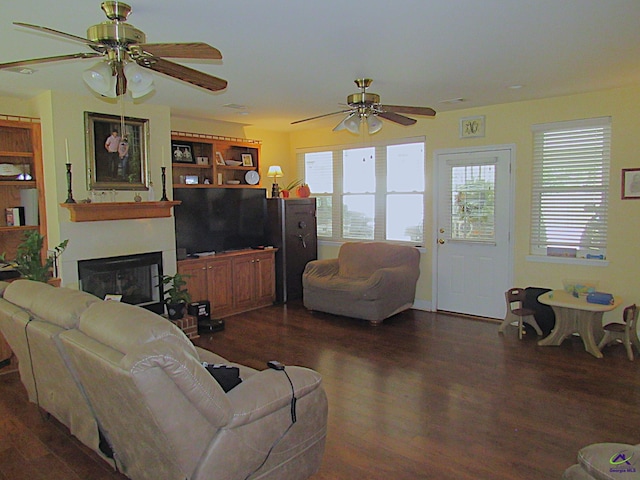 living room with dark wood-style floors, a glass covered fireplace, a ceiling fan, and a healthy amount of sunlight