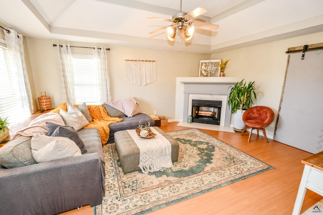 living room featuring ceiling fan, wood finished floors, a fireplace, and a raised ceiling