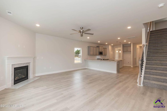 unfurnished living room with visible vents, a premium fireplace, stairs, light wood-type flooring, and recessed lighting