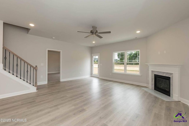 unfurnished living room with recessed lighting, light wood-style flooring, stairs, and a high end fireplace