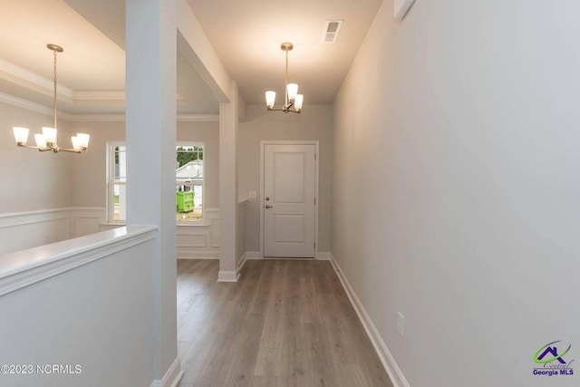 entryway featuring a wainscoted wall, visible vents, light wood-style floors, an inviting chandelier, and crown molding