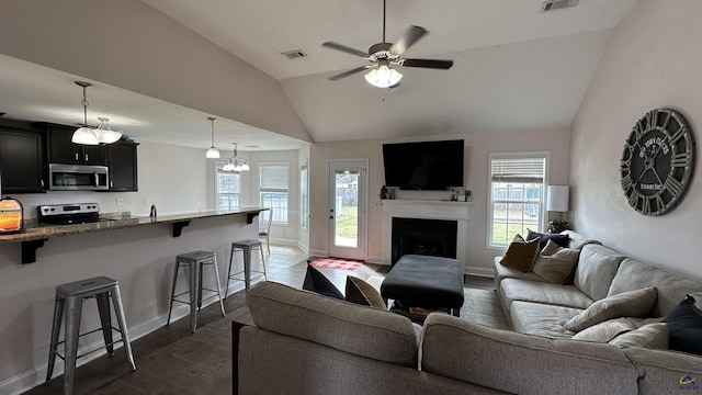 living room featuring ceiling fan, a fireplace, visible vents, vaulted ceiling, and dark wood-style floors