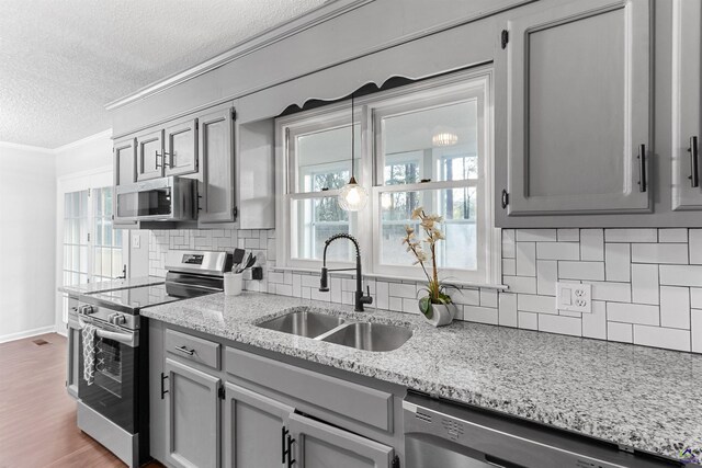kitchen featuring a textured ceiling, stainless steel appliances, a sink, ornamental molding, and gray cabinets