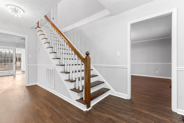 stairway with visible vents, a textured ceiling, baseboards, and wood finished floors
