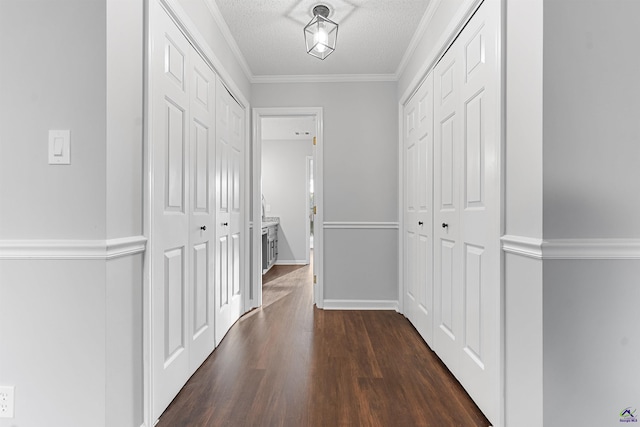 hallway featuring a textured ceiling, ornamental molding, dark wood-style flooring, and baseboards