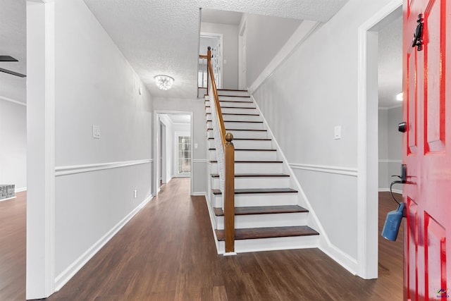 stairway with a textured ceiling, wood finished floors, visible vents, and baseboards