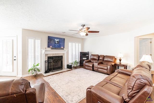 living area featuring a textured ceiling, ceiling fan, wood finished floors, a fireplace with flush hearth, and baseboards