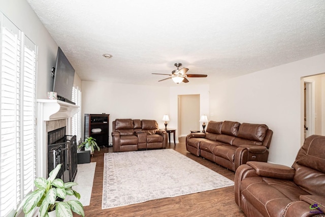 living room featuring a textured ceiling, wood finished floors, a glass covered fireplace, and a ceiling fan