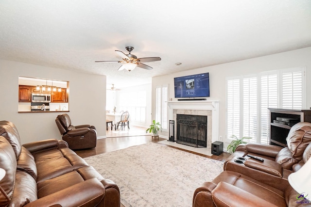 living room with ceiling fan, a textured ceiling, a premium fireplace, and wood finished floors