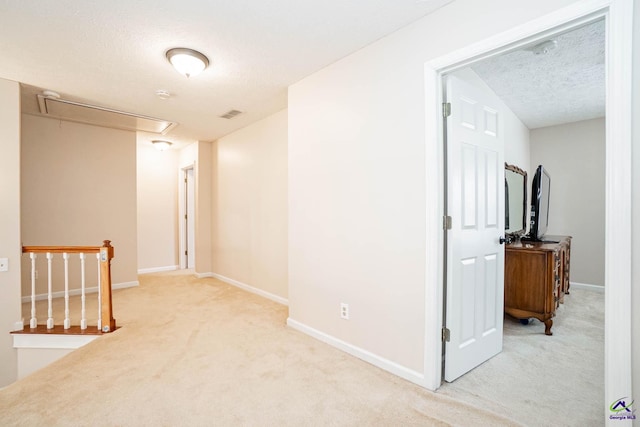 hallway with a textured ceiling, light colored carpet, visible vents, an upstairs landing, and attic access