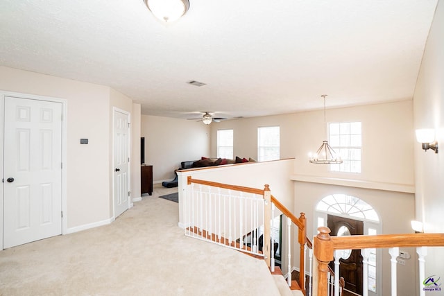 hallway featuring visible vents, baseboards, carpet, an upstairs landing, and a notable chandelier