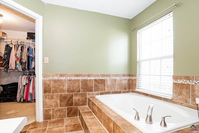 full bathroom with a garden tub, a walk in closet, a textured ceiling, and tile patterned floors