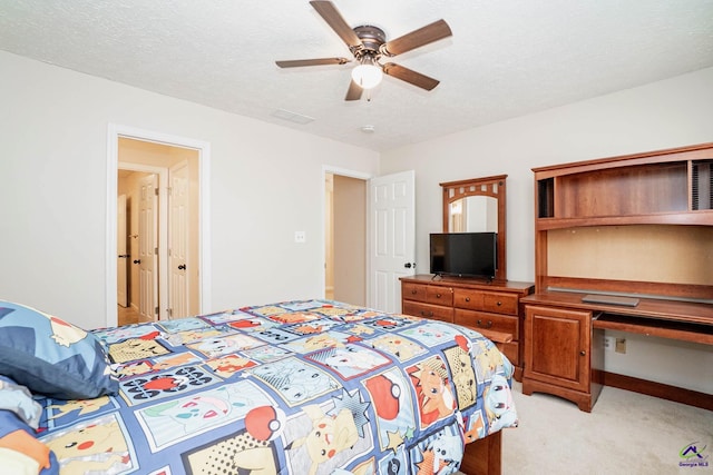 bedroom featuring a textured ceiling, ceiling fan, light colored carpet, visible vents, and built in desk