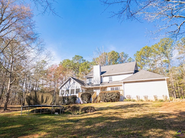 back of property featuring a trampoline, a chimney, a yard, and a deck