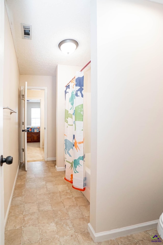 hallway with a textured ceiling, light tile patterned floors, visible vents, and baseboards