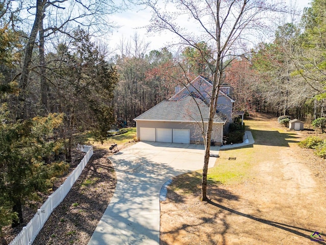 view of side of property featuring a garage, driveway, a forest view, and fence