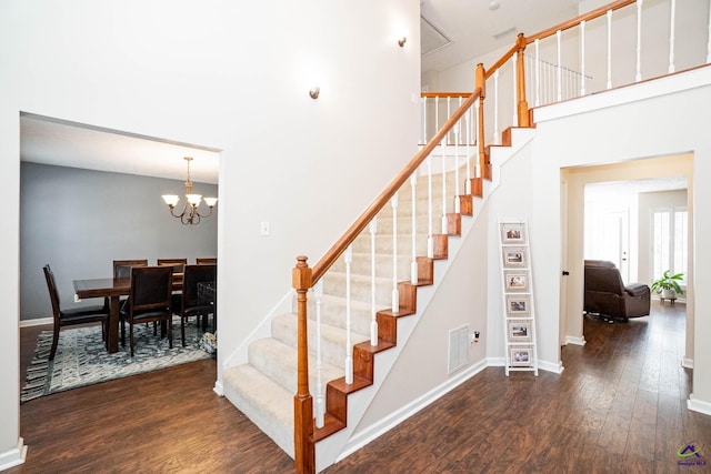 stairway featuring baseboards, wood finished floors, visible vents, and a notable chandelier