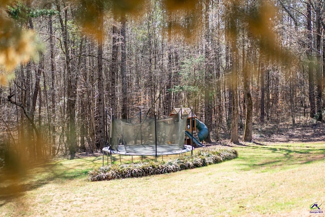 view of home's community featuring a trampoline, a playground, a yard, and a view of trees