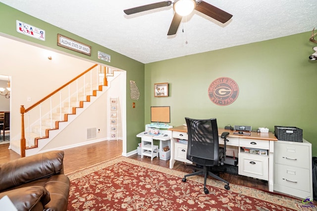 office space featuring visible vents, a textured ceiling, wood finished floors, baseboards, and ceiling fan with notable chandelier