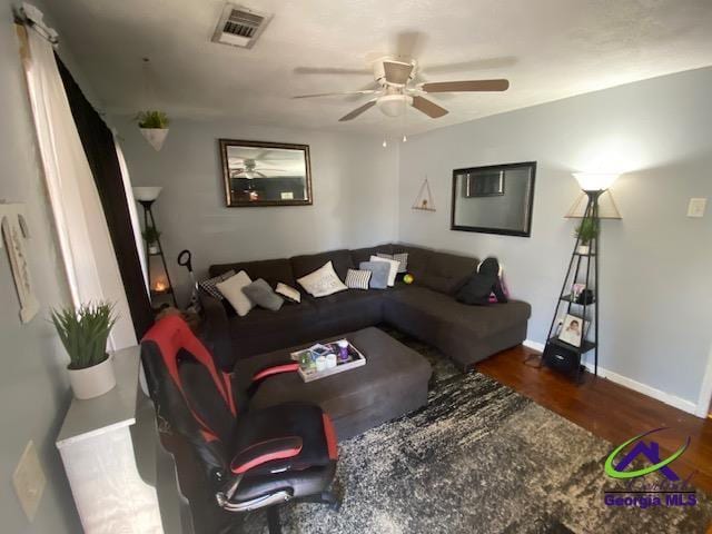 living area with baseboards, wood finished floors, visible vents, and ceiling fan