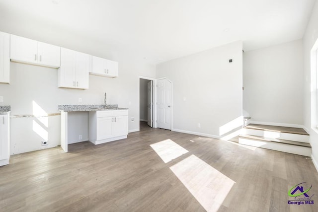 kitchen featuring light stone counters, white cabinets, light wood-type flooring, and baseboards