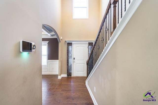 foyer entrance with arched walkways, coffered ceiling, a healthy amount of sunlight, and wood finished floors