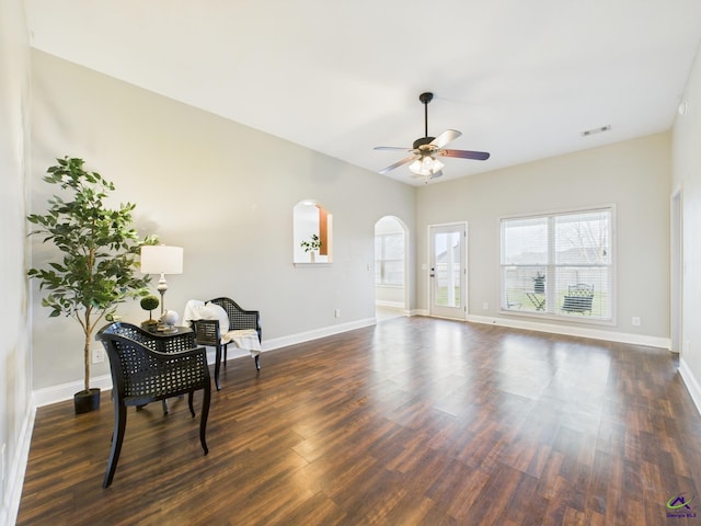 sitting room featuring visible vents, dark wood-type flooring, a ceiling fan, arched walkways, and baseboards